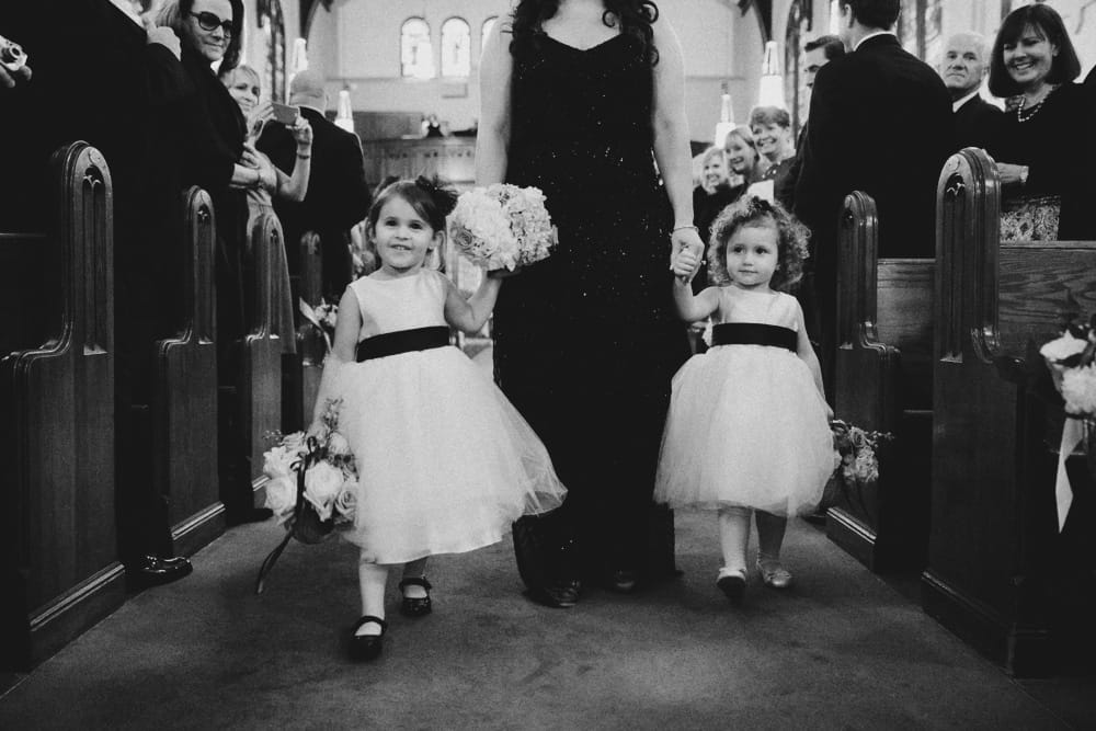 A documentary photograph of flower girls walking down the aisle of the St Augustin's Church during a Newport, Rhode Island Wedding
