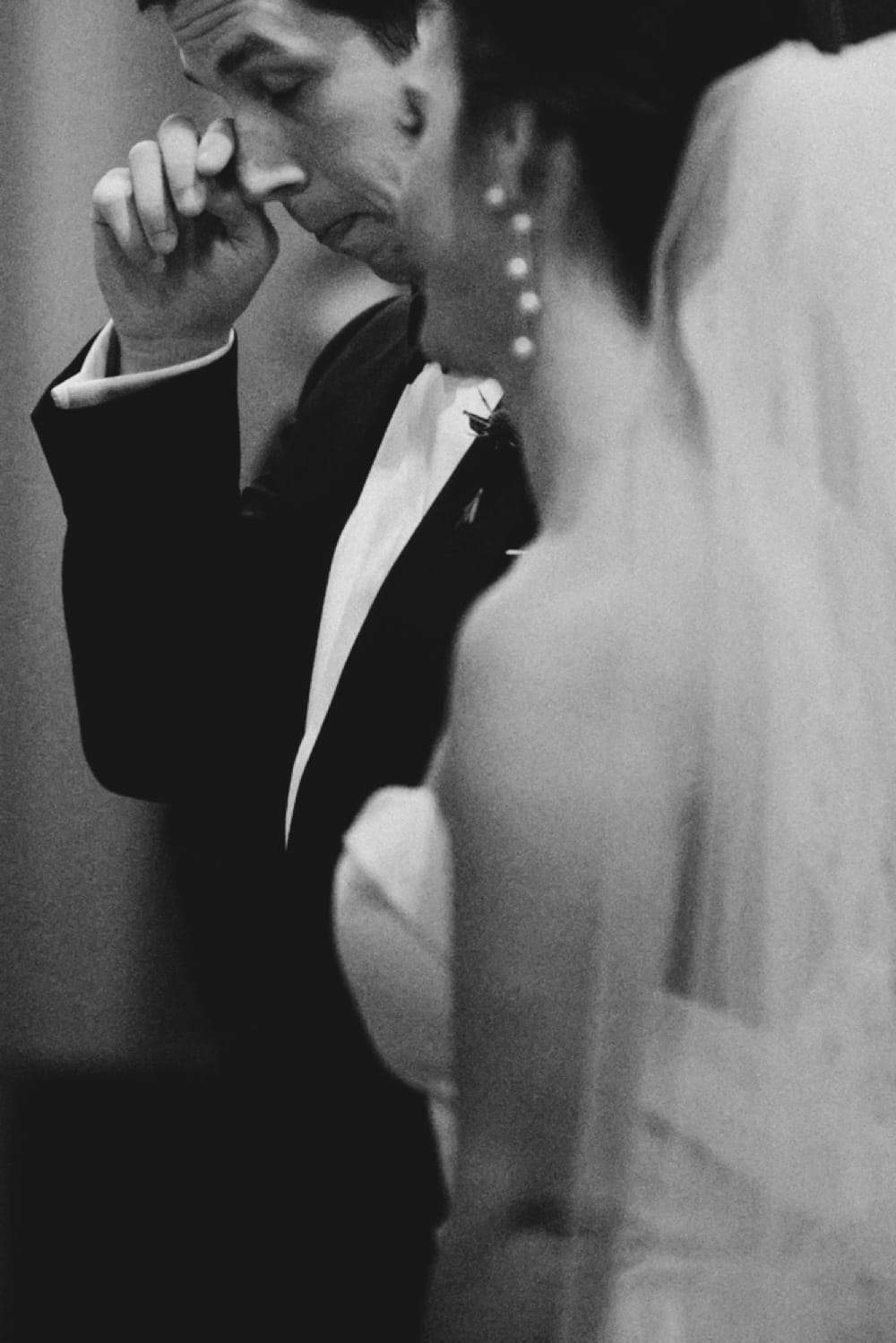 A photojournalistic portrait of a groom wiping away a tear during his wedding ceremony at St. Augustin's Church in Newport, Rhode Island