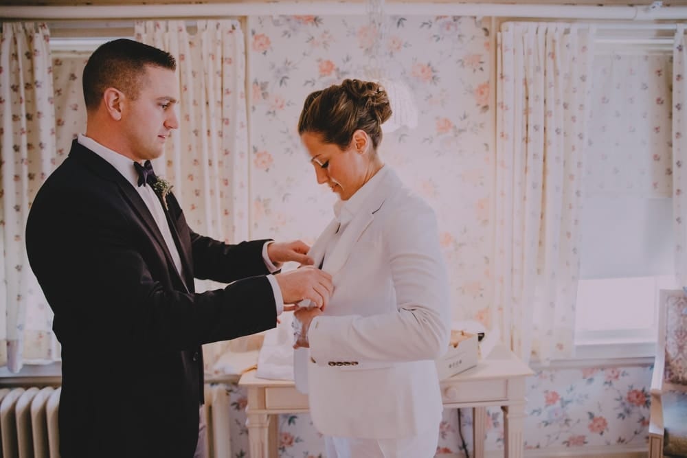 A brides best man helps her button her jacket at the Governors Inn before her rustic New Hampshire barn wedding at Kitz Farm