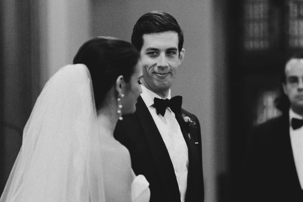 A photojournalistic portrait of groom smiling at his bride during their wedding ceremony at St. Augustin's Church in Newport, Rhode Island