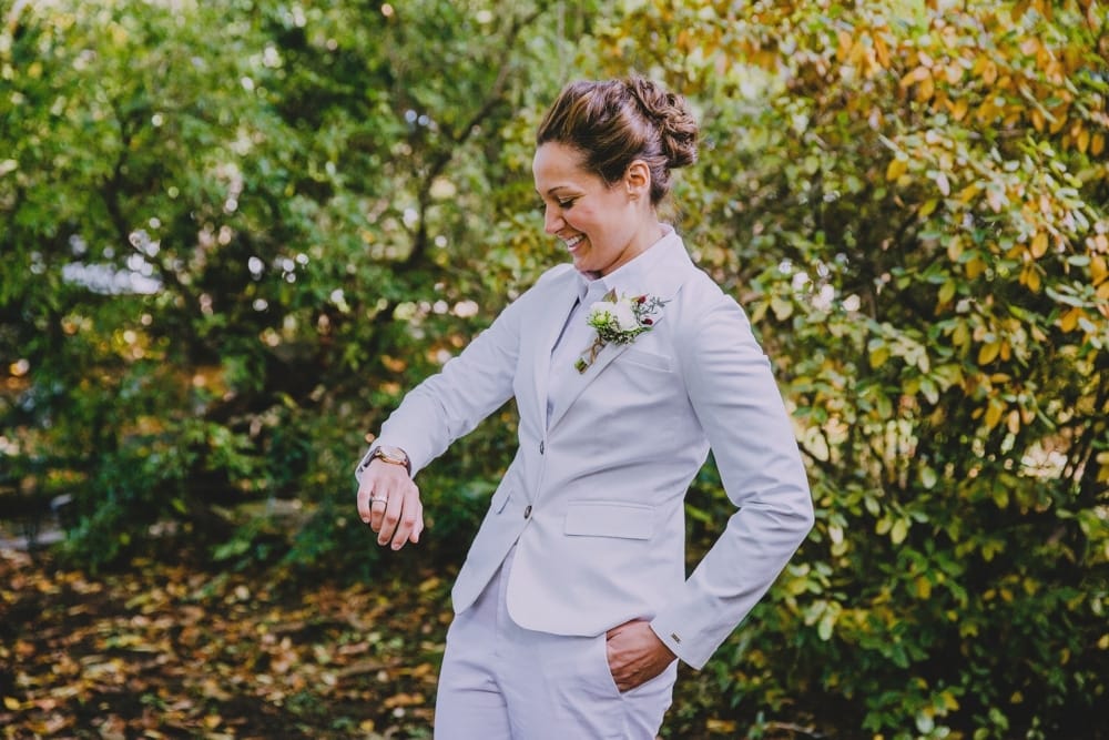 A bride looks at her watch as she waits for her bride to arrive for their first look before their rustic barn wedding at Kitz Farm in New Hampshire
