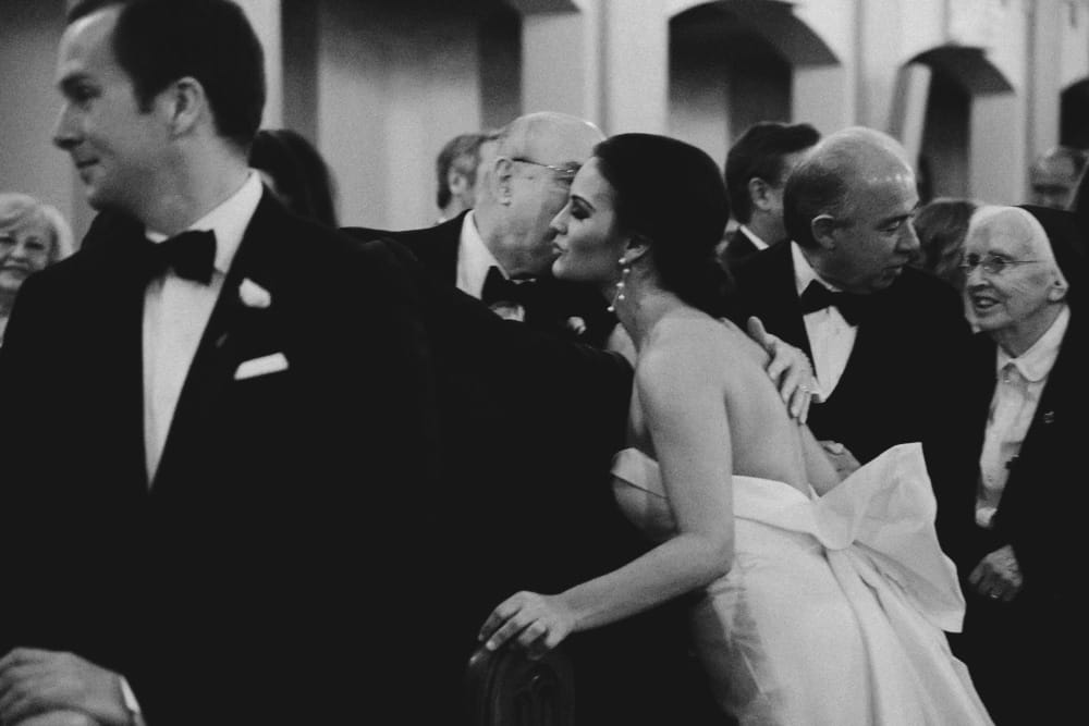 A documentary photograph of a bride kissing her father in law during her wedding ceremony at St. Augustin's Church in Newport, Rhode Island