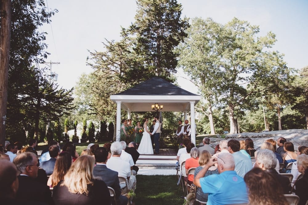 A photojournalistic photograph of a bride and groom saying their vows during an intimate and rustic outdoor ceremony at a River Club Wedding in Scituate, Massachusetts