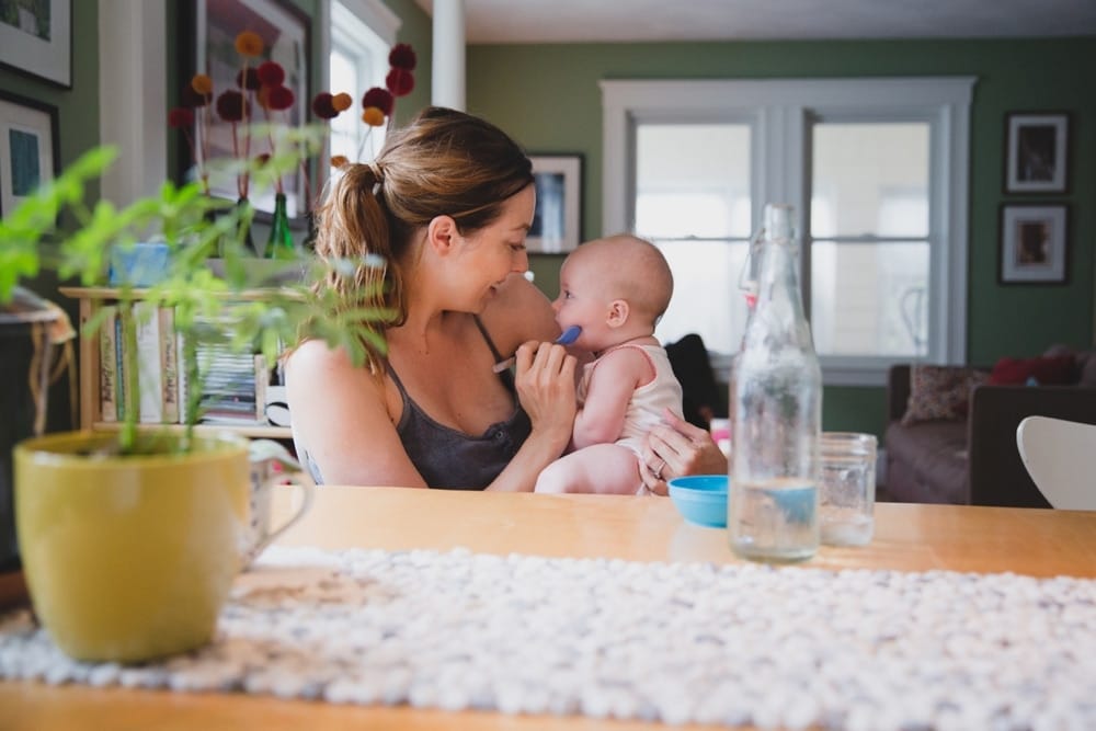 A documentary photograph of a mother feeding her baby during an in home family session in Boston, Massachusetts