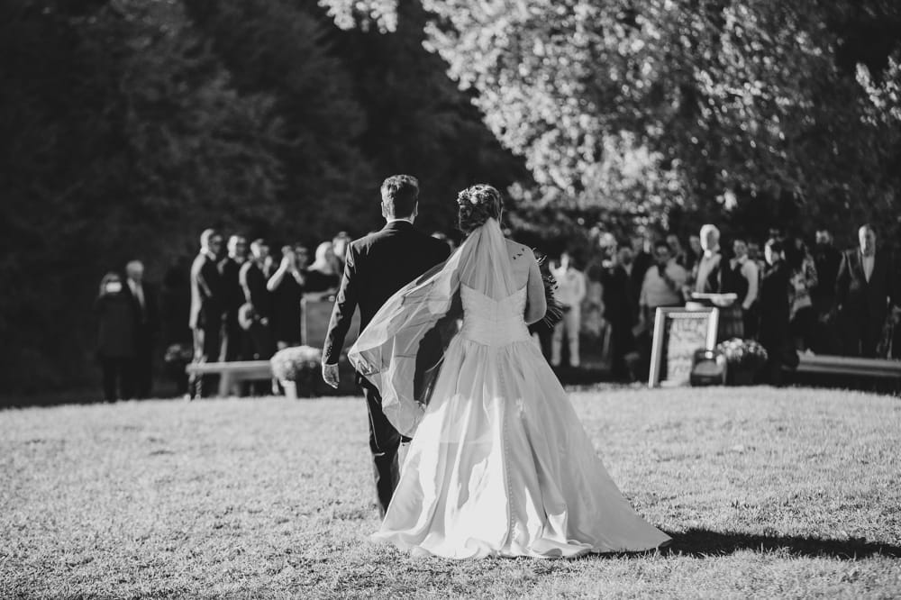 A documentary photograph of a bride walking down the aisle with her father at Kitz Farm during her rustic outdoor New Hampshire wedding ceremony