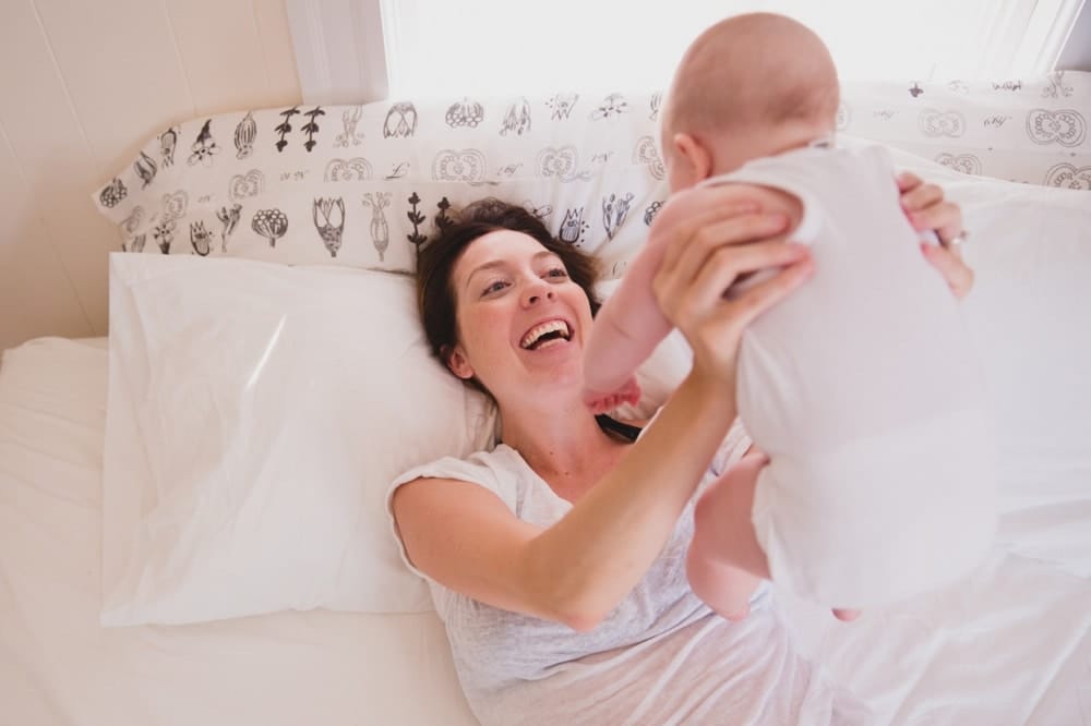 An intimate documentary photograph of a mother playing with her baby in the bed during their in home family photography session in Boston, Massachusetts