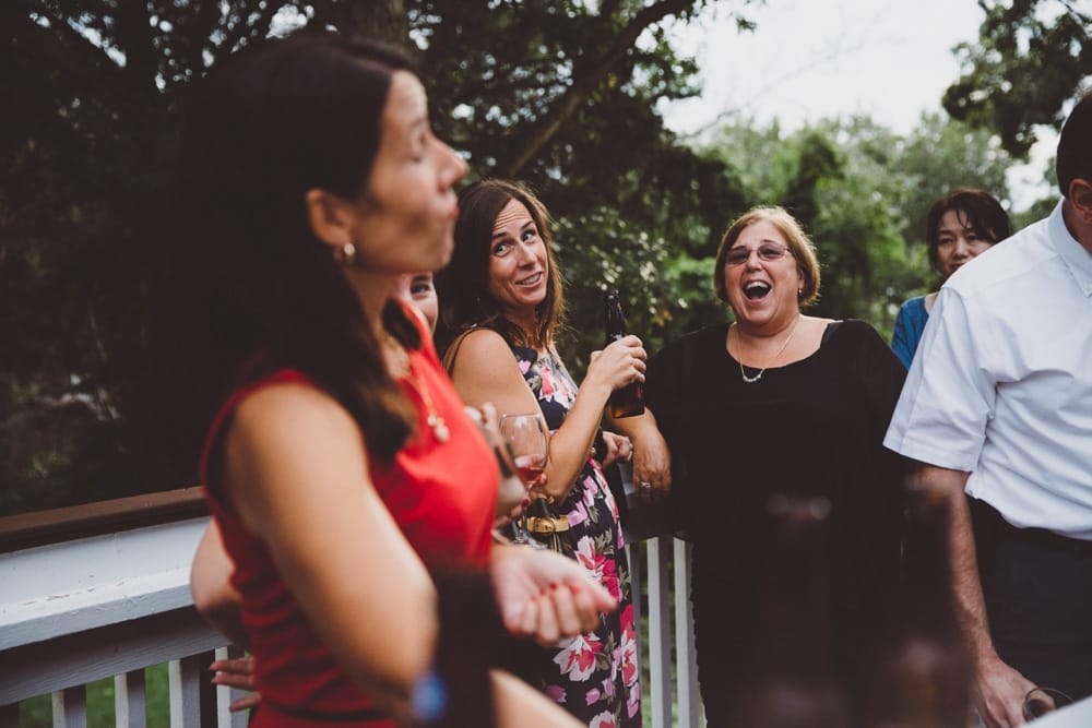 A photojournalistic photograph of wedding guests talking and laughing during a rustic and relaxed outdoor River Club Wedding in Scituate, Massachusetts