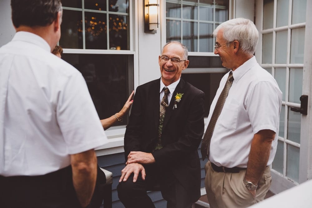 A photojournalistic photograph of at the father of the bride laughing with friends during a relaxed and rustic outdoor River Club Wedding in Scituate, Massachusetts