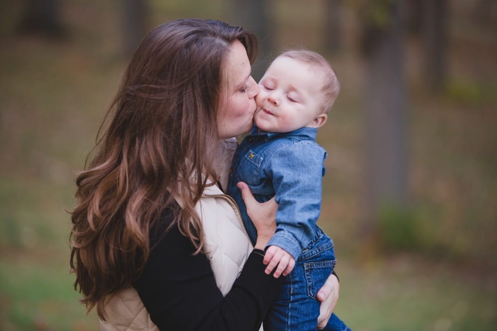 A beautiful and intimate photograph of a mother kissing her baby boy during a lifestyle family photo session in the Arnold Arboretum of Boston, Massachusetts