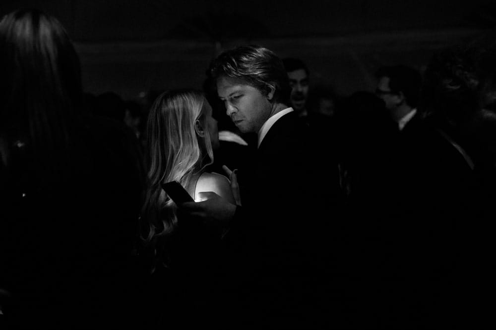 A documentary photograph of a wedding guest looking at his phone during a wedding reception at the Castle Hill Inn in Newport, Rhode Island