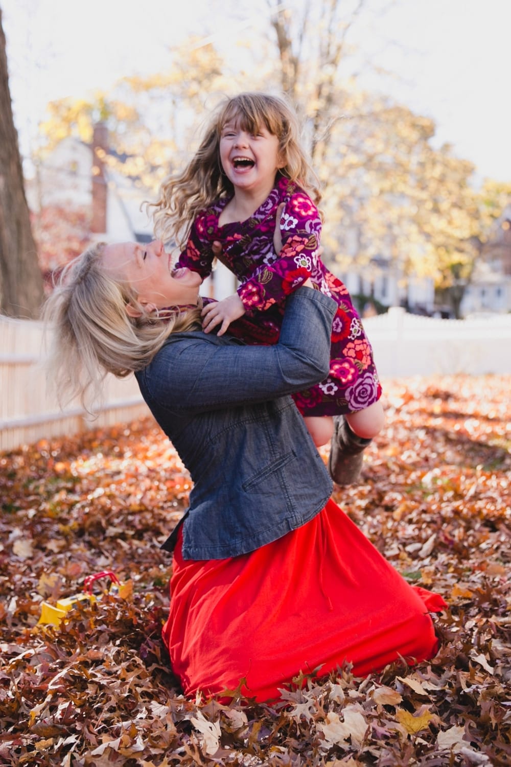 A fun documentary photograph of a mother playing in the leave with her daughter during a fall lifestyle family photo session at home in Boston, Massachusetts