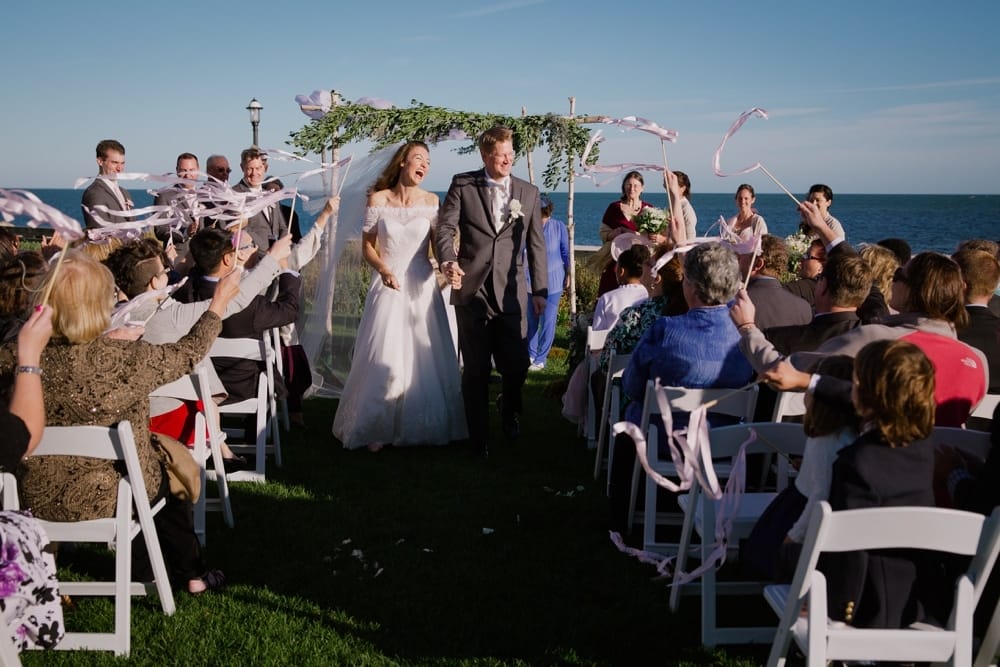 A photojournalistic photograph of a couple laughing as they walk down the aisle after being pronounced husband and wife at their outdoor wedding ceremony on Cape Cod