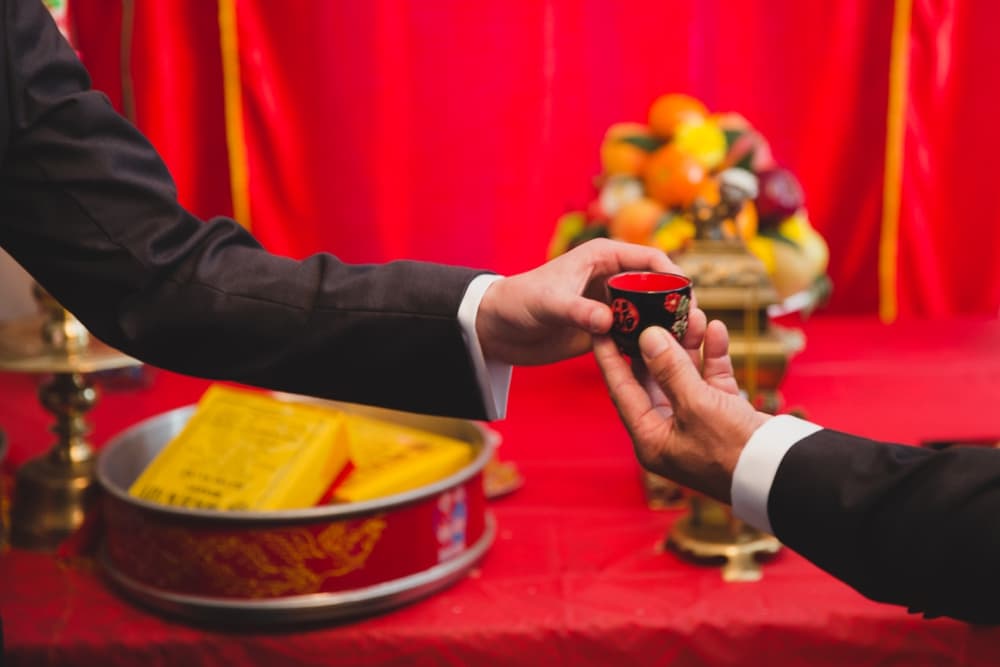 A photojournalistic photograph of a groom handing his father a cup of tea during his vietnamese tea ceremony in Boston, Massachusetts