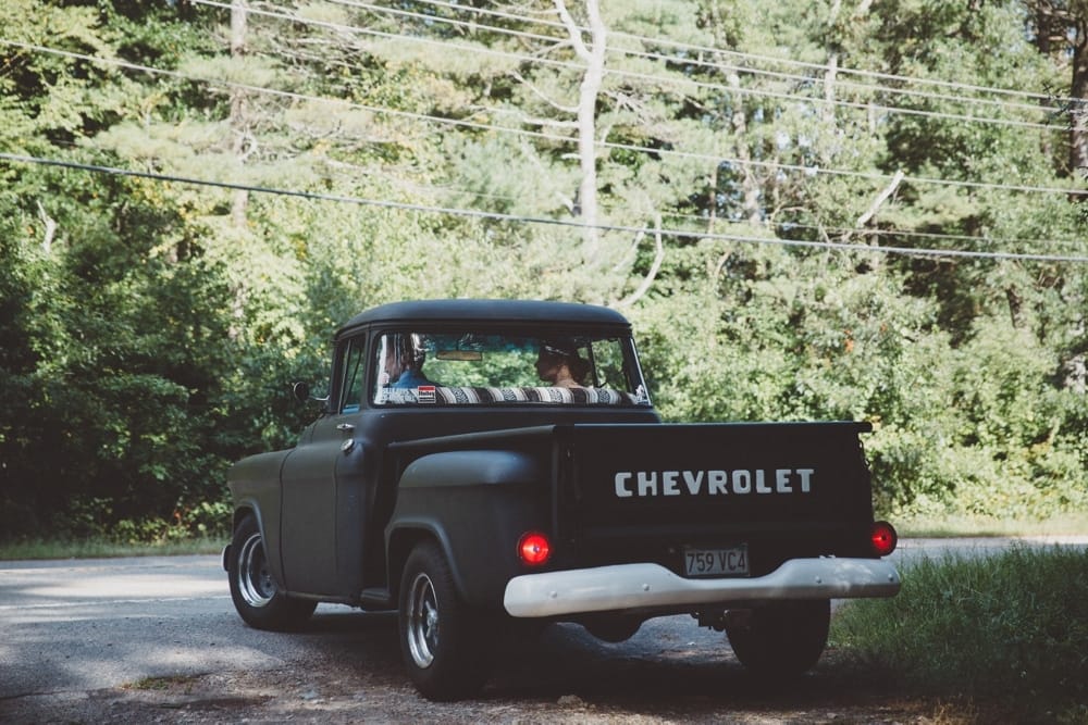 A documentary photograph of a bride and groom driving to the wedding at the River Club in a vintage Chevrolet truck before their wedding in New Hampshire