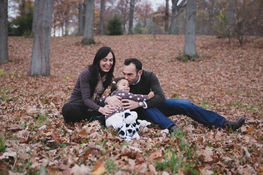 A lifestyle photograph of a father kissing his daughter during a fall mini session at the Arnold Arboretum in Boston, Massachusetts