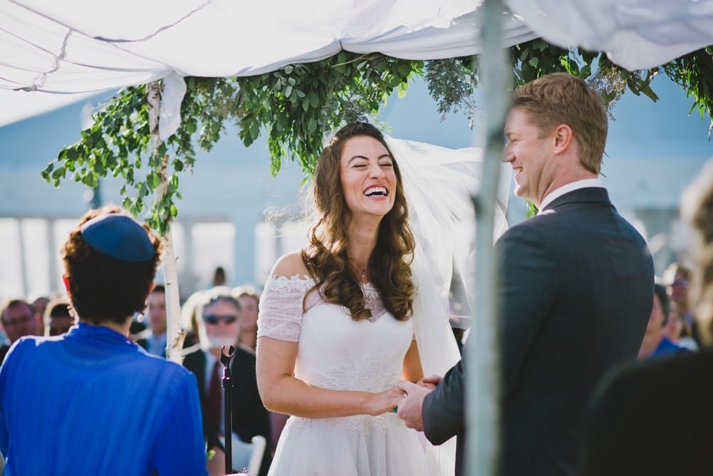 A photojournalistic photograph of a bride and groom laughing during their outdoor jewish wedding ceremony in Cape Cod, Massachusetts