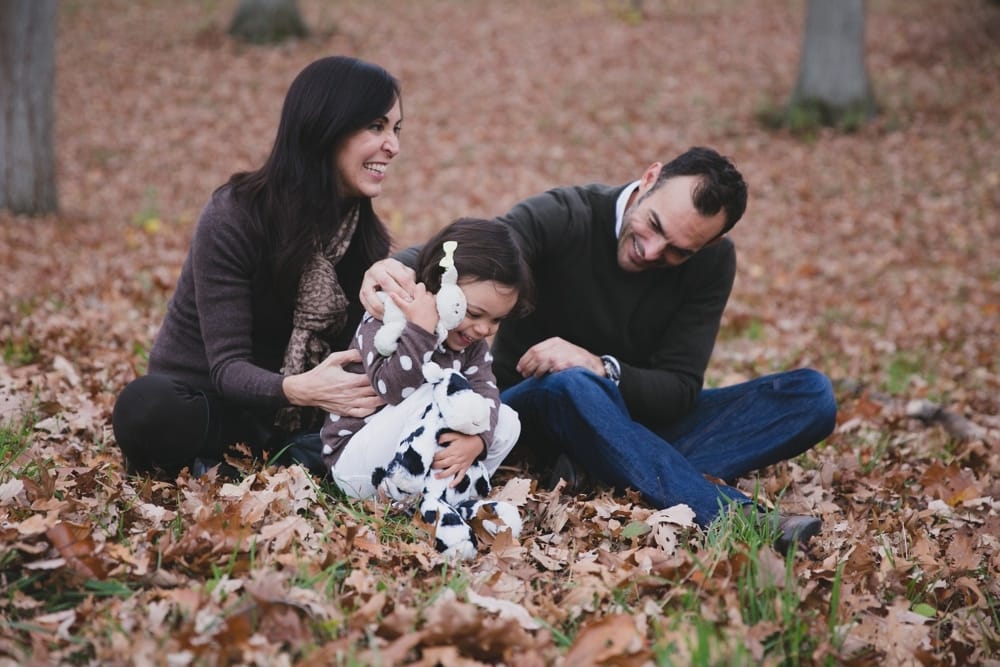 A fun lifestyle photograph of a family playing in the fallen leaves during their fall mini session at the Arnold Arboretum in Boston, Massachusetts