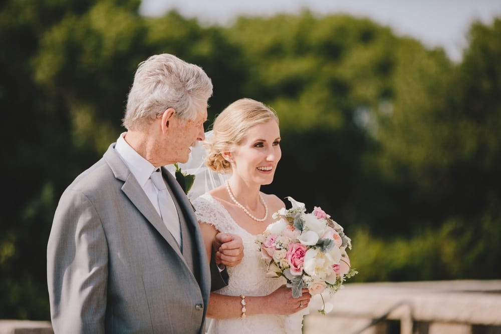 A documentary photograph of a bride walking down the aisle with her father during an outdoor wedding ceremony at Cape Cod's Pilgrim's Monument in Provincetown, Massachusetts