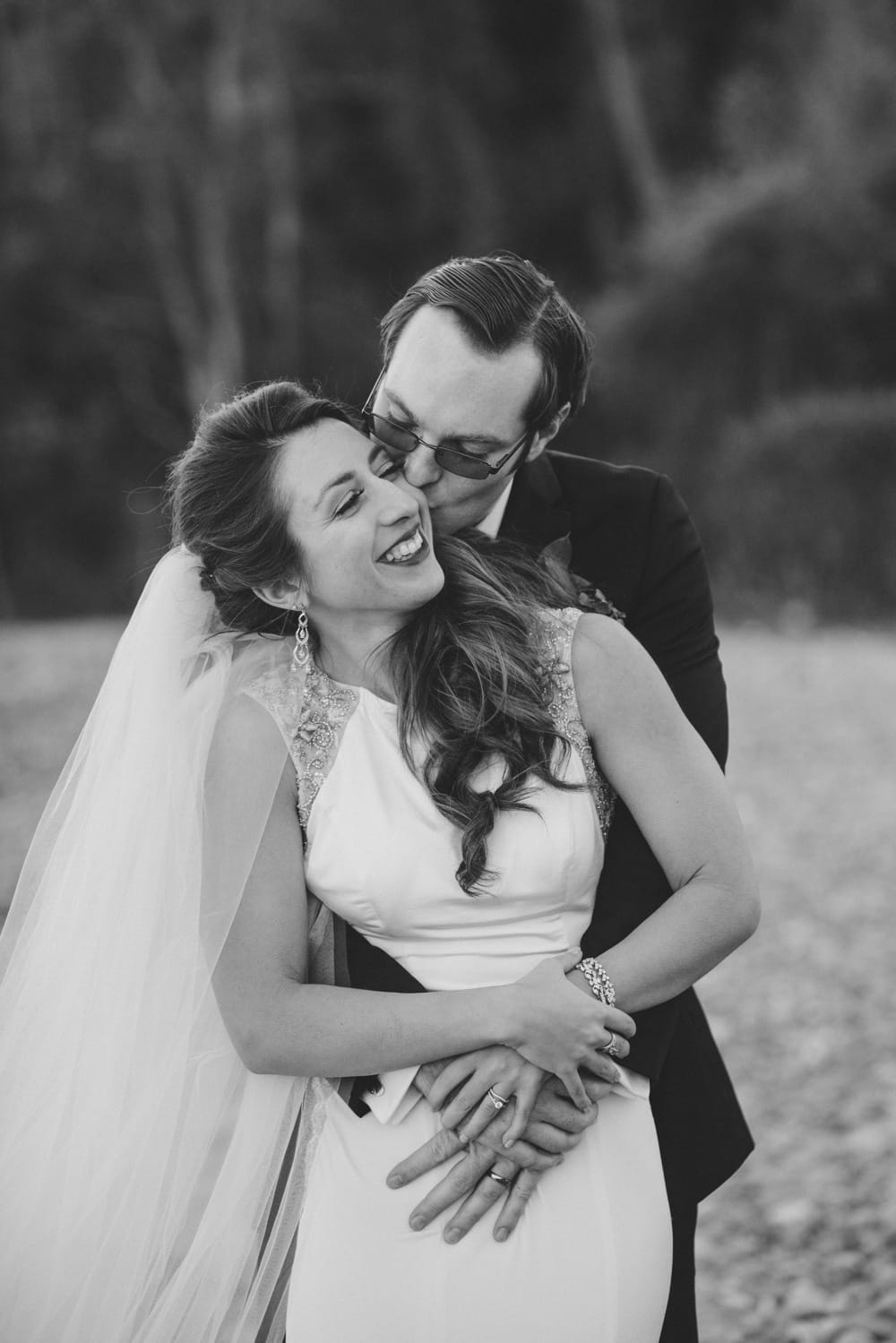 A natural and relaxed photograph of a bride and groom sharing a kiss and a cuddle during their seaside wedding at the Oceanview of Nahant in Massachusetts