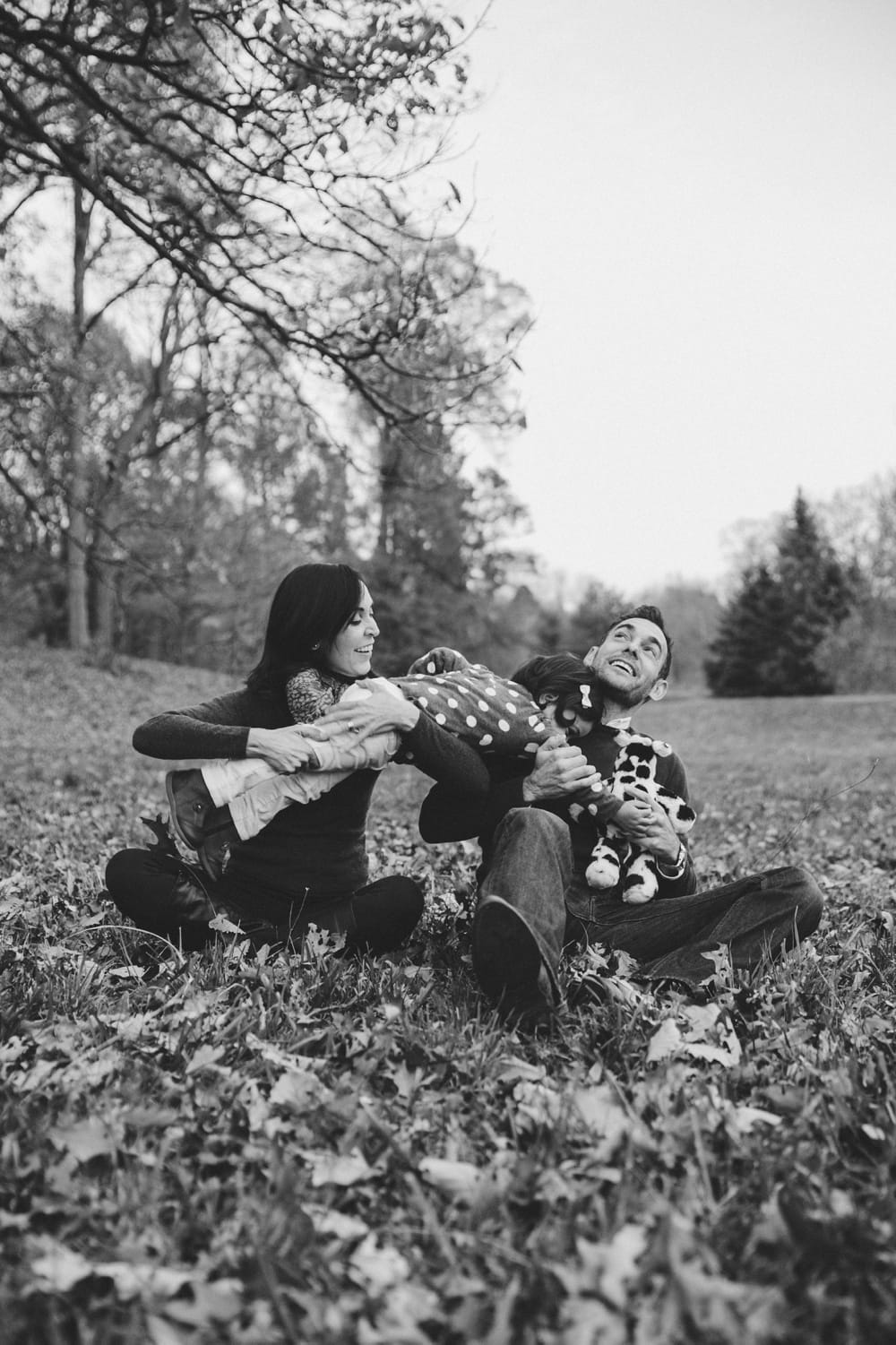 A fun lifestyle photograph of a family playing in the fallen leaves during a fall mini session at Boston's Arnold Arboretum in Jamaica Plain, Massachusetts
