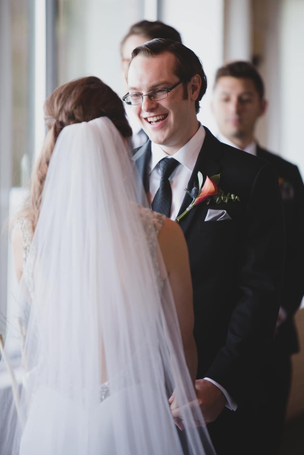 A documentary photograph of groom smiling at his bride during their intimate wedding ceremony at the Oceanview of Nahant in Massachusetts