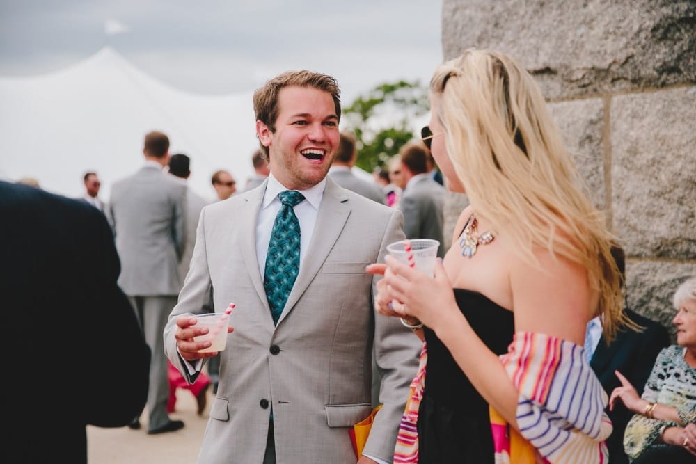 A photojournalistic photograph of wedding guest talking and laughing during a fun, summer Cape Cod wedding at Pilgrim's Monument in Provincetown, Massachusetts