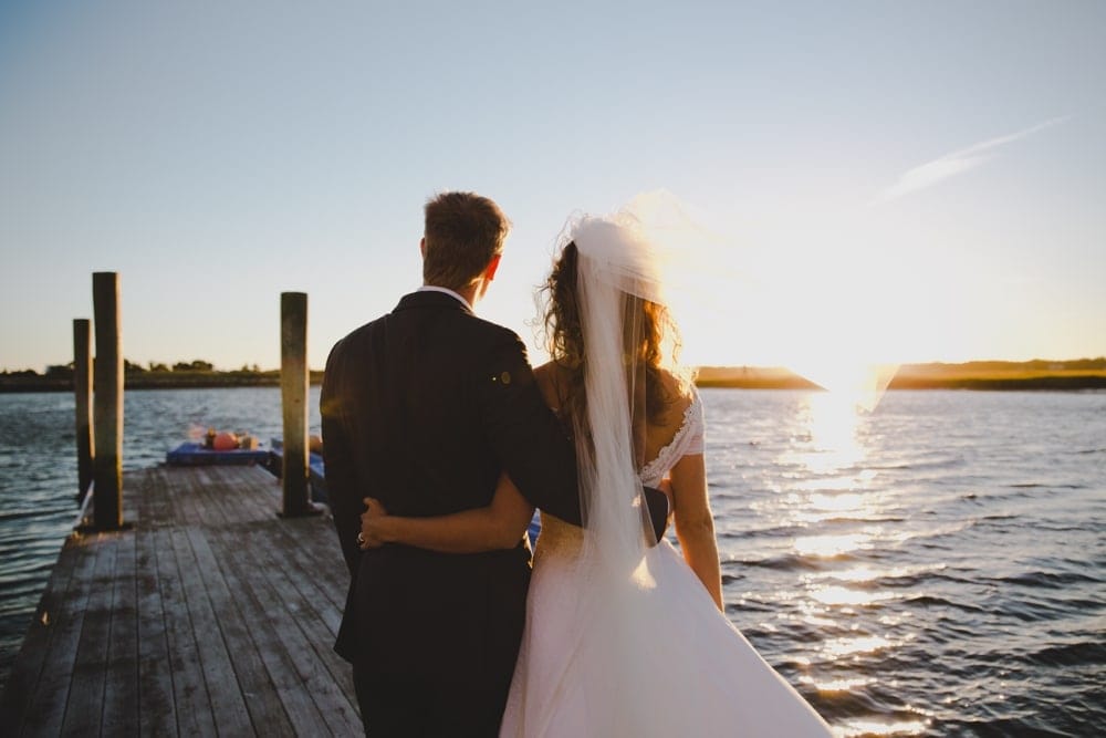 An artistic and natural portrait of a bride and groom looking out at the sunset during their summer wedding on Cape Cod