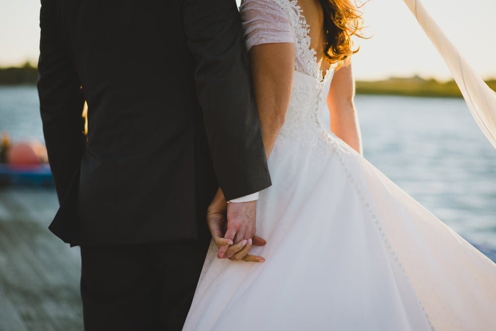 An artistic and intimate photograph of a bride and groom holding hands during their summer wedding on Cape Cod