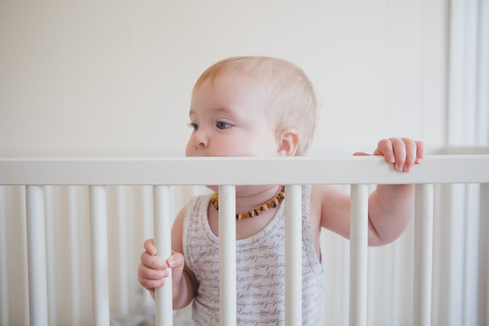 A lifestyle photograph of a baby girl standing in her crib during an in home lifestyle session in Boston