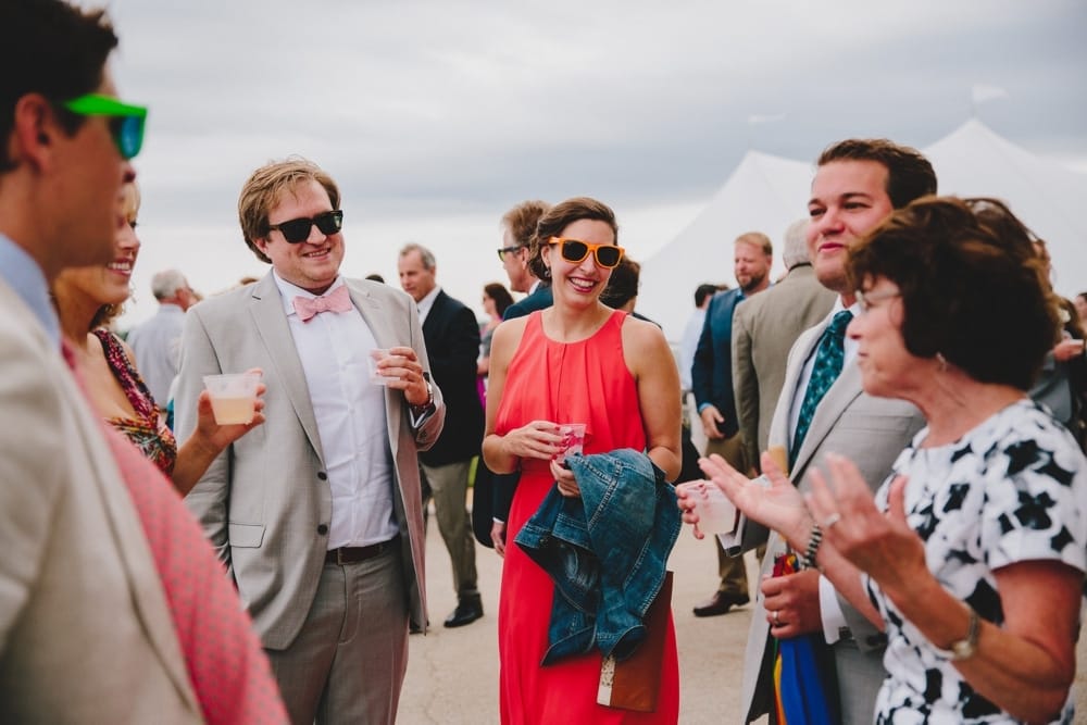 A photojournalistic photograph of wedding guests enjoying cocktail hour during a fun summertime wedding at Cape Cod's Pilgrim's Monument in Provincetown, Massachusetts