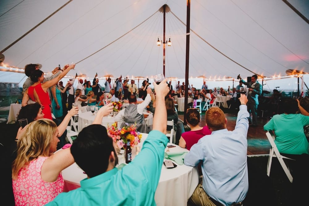 A documentary photograph of wedding guest toasting the bride and groom during a fun, summertime Cape Cod wedding at Pilgrim's Monument in Provincetown, Massachusetts