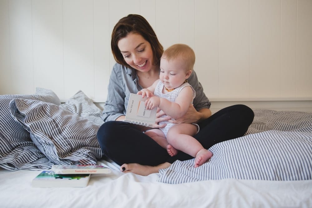 A documentary photograph of a mother reading a book to her baby girl during their in home lifestyle session in Boston