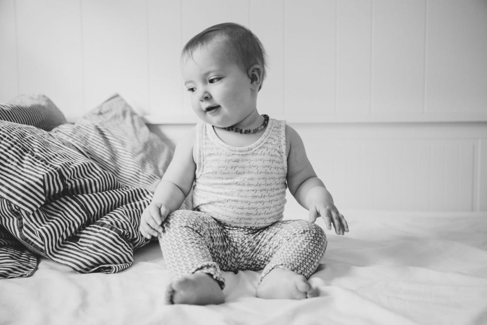 A lifestyle photograph of a baby girl sitting on a bed during an in home lifestyle session in Boston