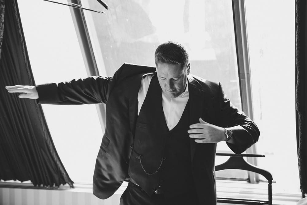 A photojournalistic photograph of a groom putting on his suit at the Langham Hotel before his State Room Wedding in Boston