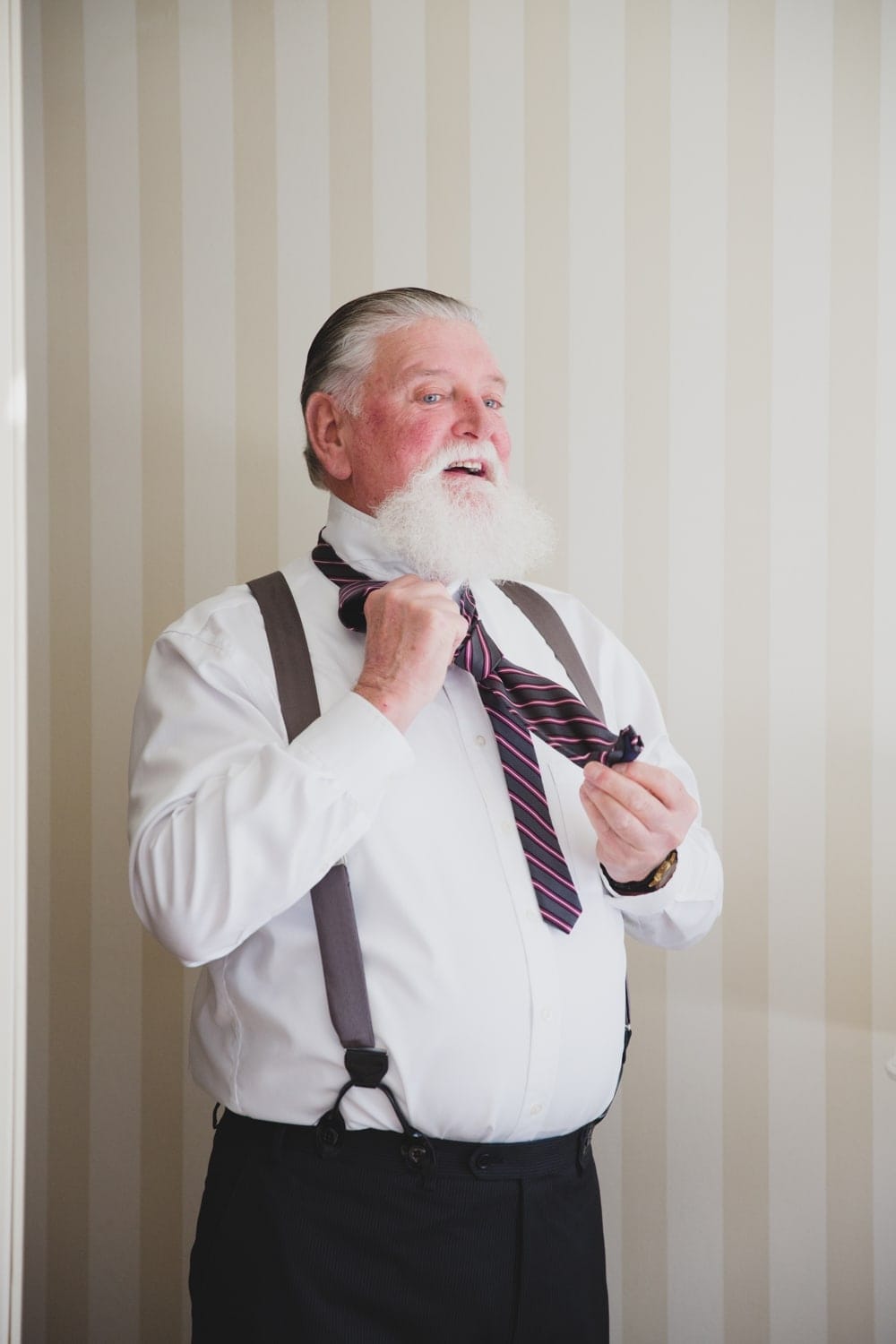A photojournalistic photograph of the Groom's father putting on his tie at the Langham hotel before his son's State Room Wedding in Boston
