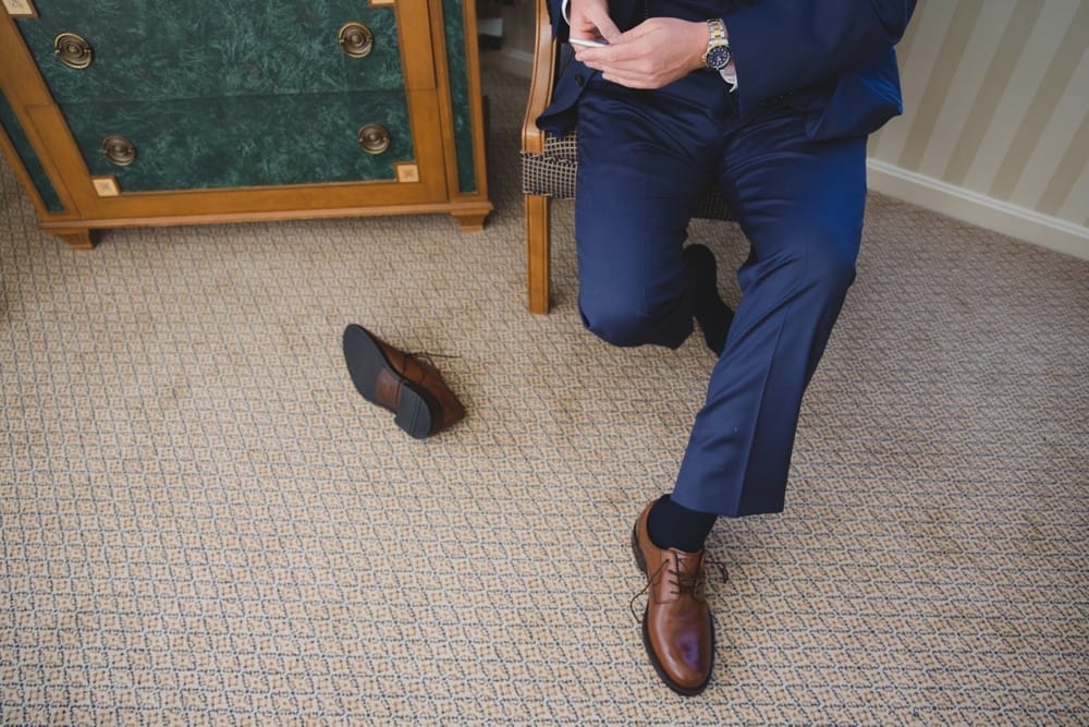A photojournalistic photograph of a groom sending a text while putting on his shoes at the Langham Hotel before his State Room Wedding