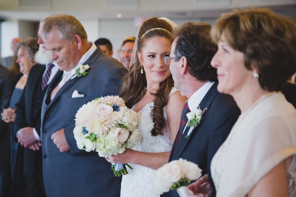A documentary photograph of a bride looking at her father as she walks up the aisle during her State Room Wedding ceremony in Boston