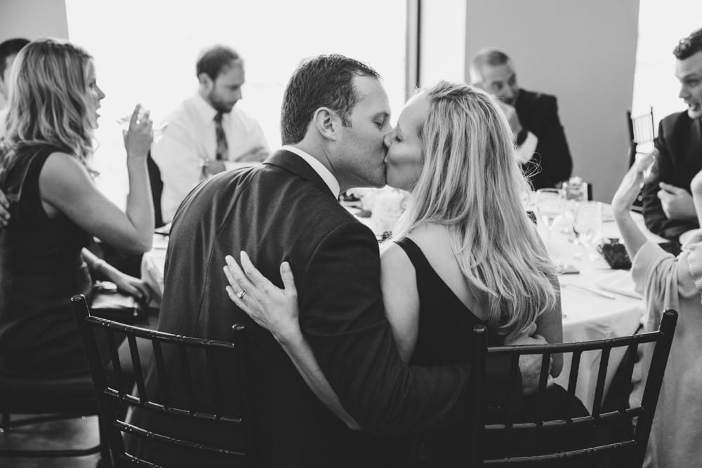A documentary photograph of a couple kissing at the dinner table during a State Room wedding in Boston