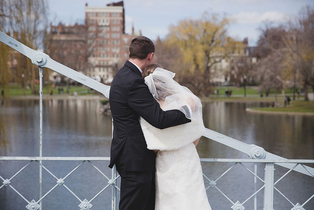 A documentary portrait of wedding couple cuddling and looking out at the view of the Boston Public Gardens during their wedding portrait session in Boston