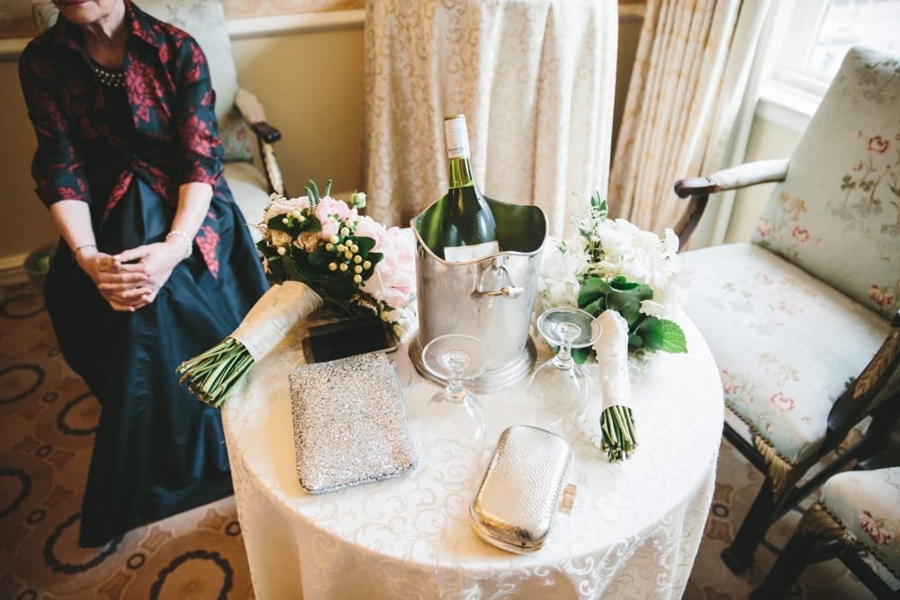A documentary photograph of a grandmother sitting by a table with wedding bouquets, hand bags, and champagne during a Taj Boston Hotel Wedding in the Back Bay
