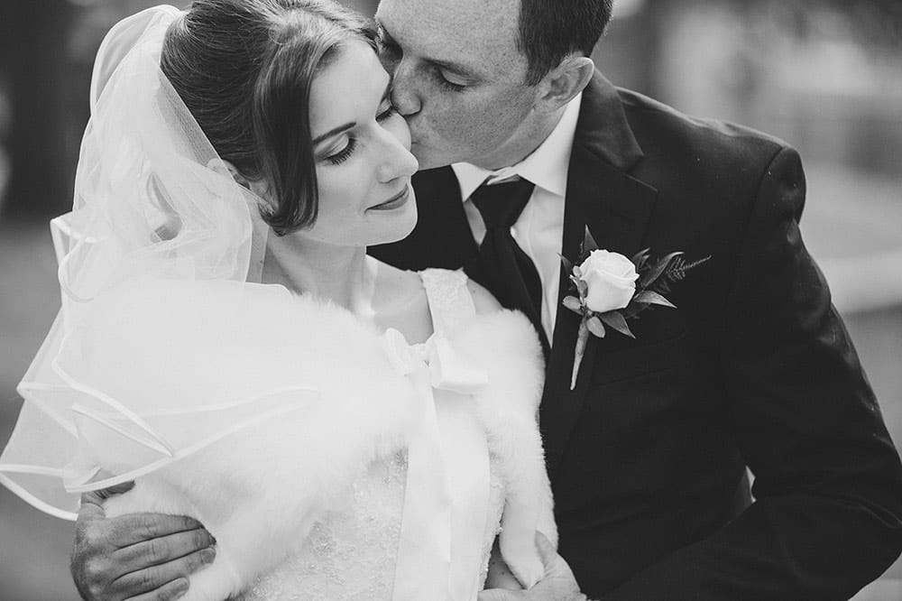 A documentary photograph of groom kissing his bride during their wedding portrait session in Boston Public Gardens
