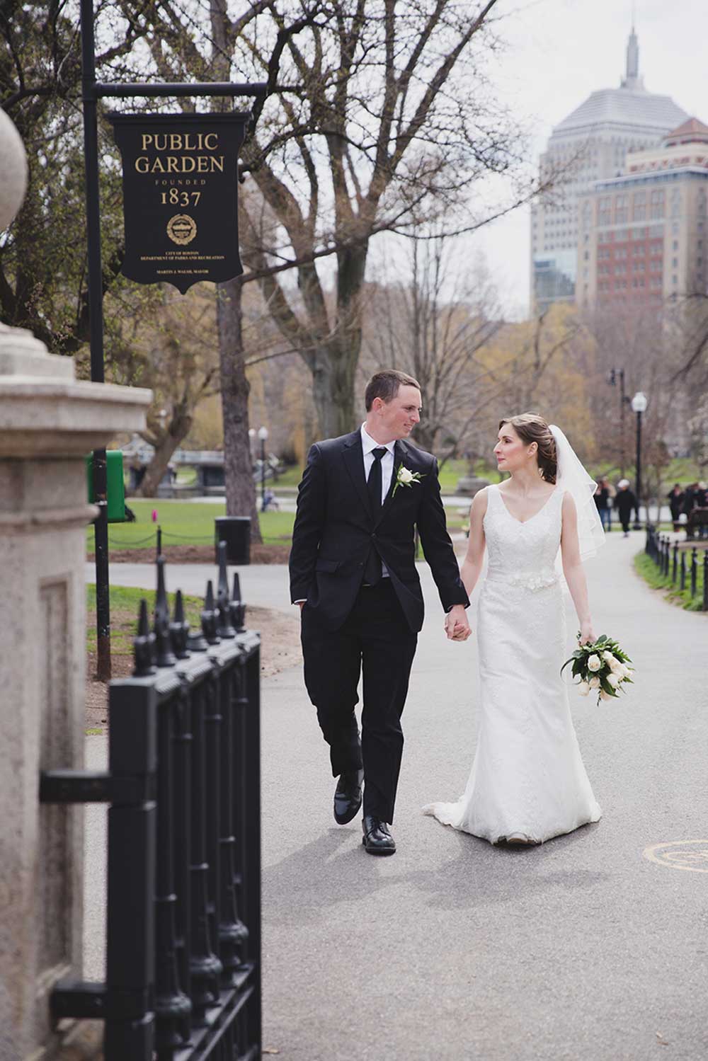 A documentary photograph of a wedding couple walking through the Boston Public Gardens during their wedding portrait session