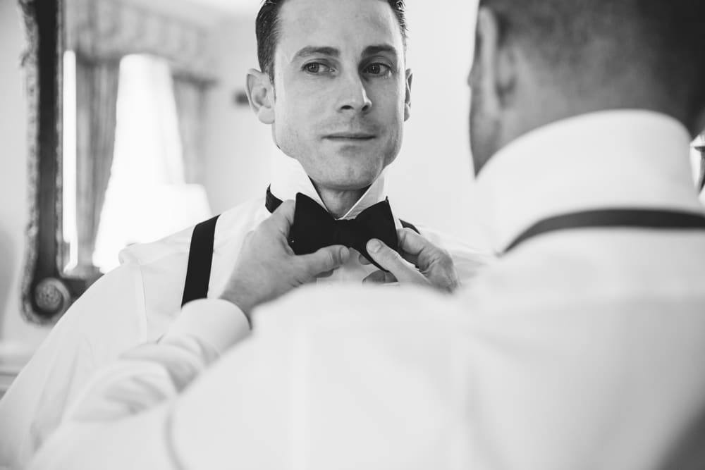 A documentary photograph of a Groomsman tying another Groomsman's bow tie before a Taj Boston Hotel Wedding in Back Bay