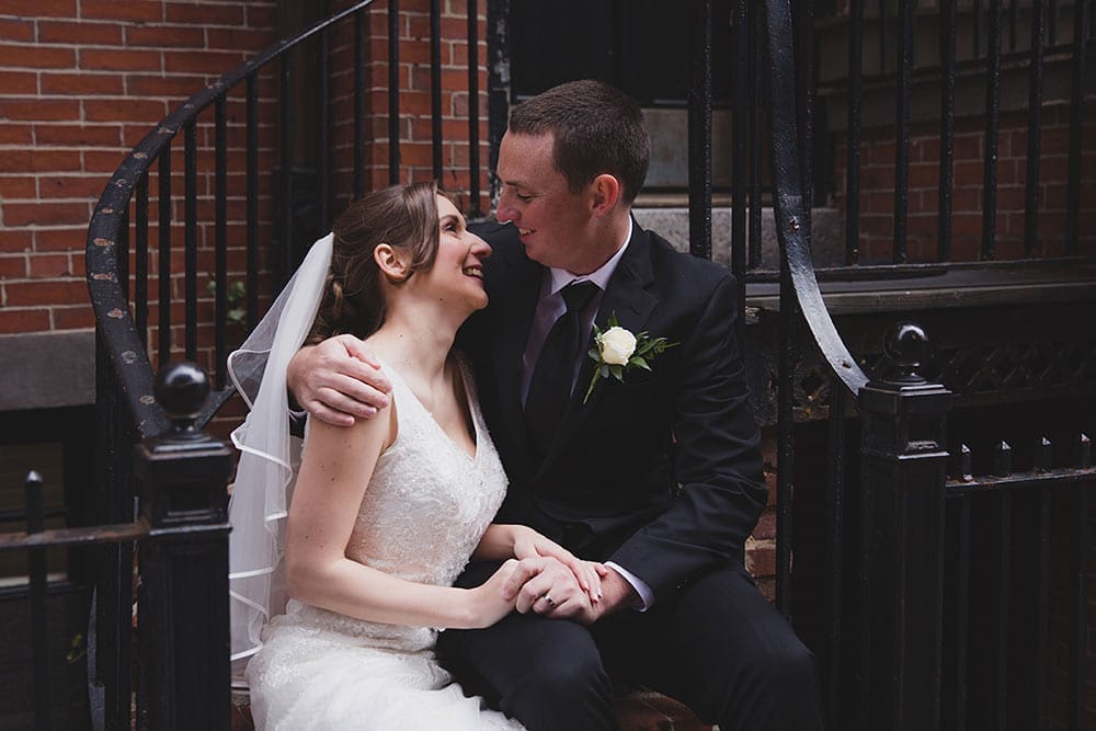 A documentary photograph of a couple laughing together as they sit on the stairs of beautiful home in Beacon Hill during their wedding portrait session