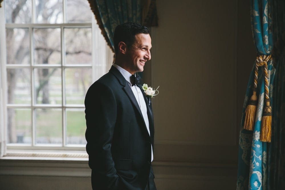 A documentary photograph of a Groom smiling as he waits for his bride to arrive to their first look at the Taj Boston Hotel before their Boston City Wedding