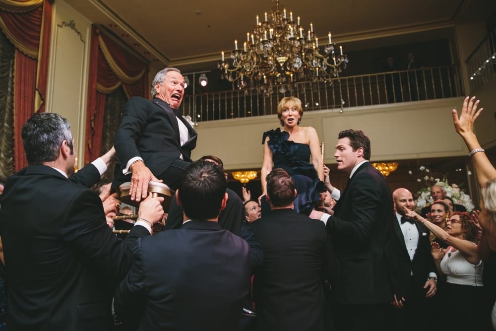 A documentary photograph of the grooms parents being lifted in their chairs during the hora at a Taj Boston Hotel Wedding