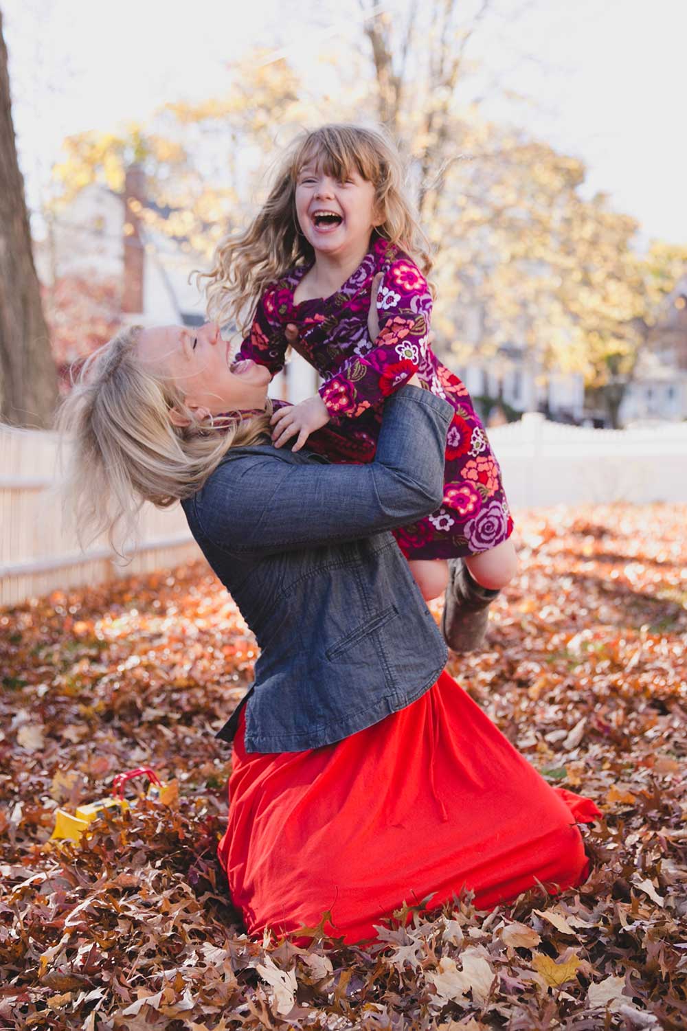 A documentary photograph showing everyday motherhood as a mother plays in the leaves with her daughter outside their home in Boston