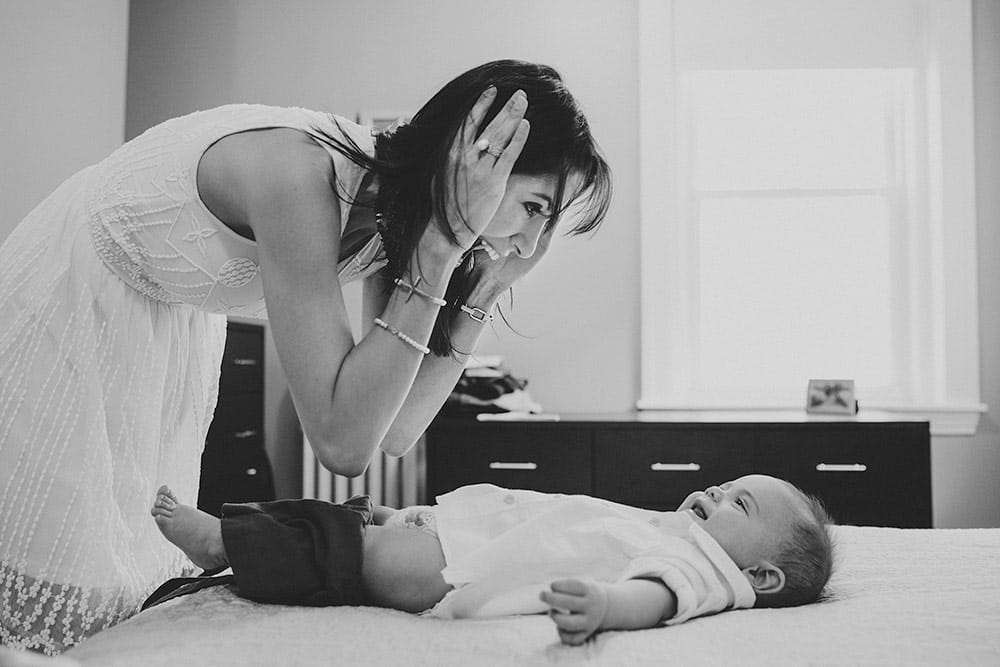 A documentary photograph depicting everyday motherhood as a mom plays peek a boo with her son while changing his clothes during an in home family session in Boston