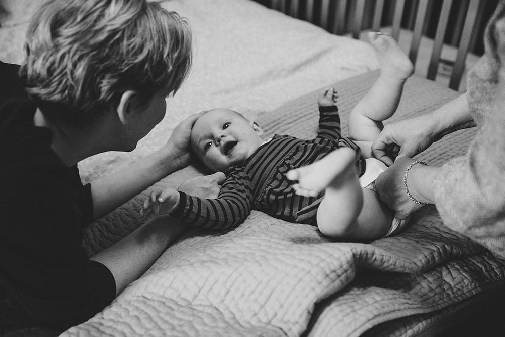 A photojournalistic photograph depicting everyday motherhood as two moms change their baby girls diaper during an in home family session in Boston