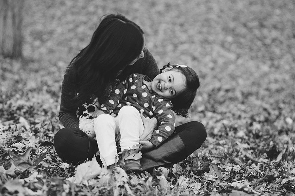 A lifestyle photograph of everyday motherhood as a mom and daughter laugh together during their fall family session in the Boston Arboretum